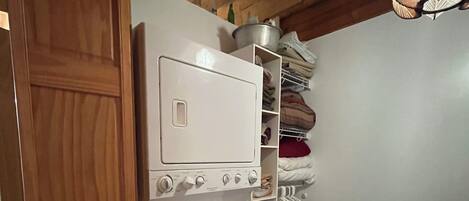 Une petite buanderie avec un lave-linge et un sèche-linge blancs, des poutres en bois au plafond et un étendoir suspendu.