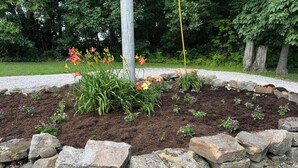 A garden bed with various plants and flowers, surrounded by a stone border. - Private, cozy cabin on 13 acres with two ponds (Bloomfield)