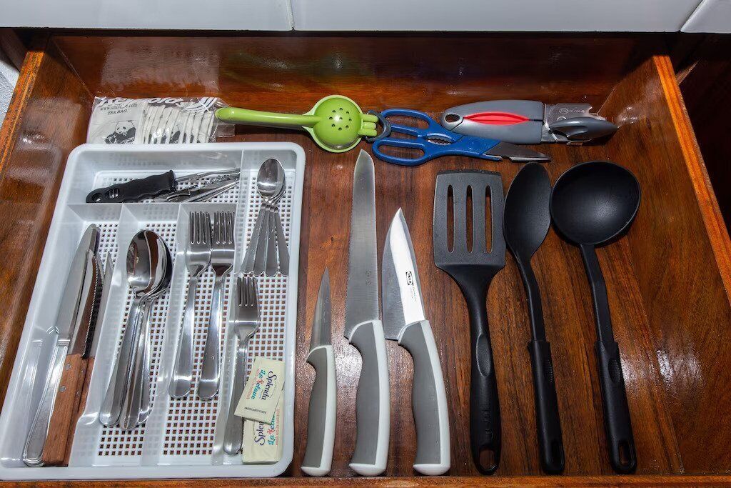 A drawer containing various kitchen utensils including a colander, scissors, a spatula, a ladle, and a tray with cutlery.