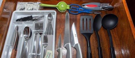 A drawer containing various kitchen utensils including a colander, scissors, a spatula, a ladle, and a tray with cutlery.