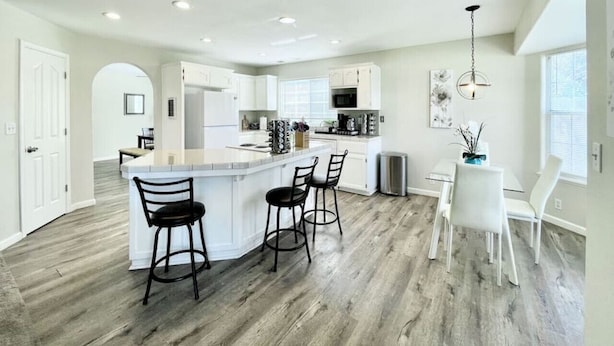 Una cocina moderna con una isla central, taburetes de bar y un comedor con mesa y sillas blancas.