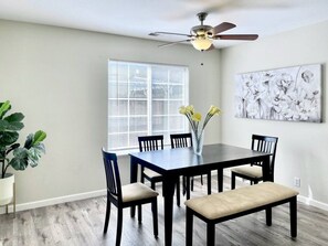 A dining area with a table, chairs, a vase with flowers, a ceiling fan, and a window with blinds. - Luxury 4BR Family Home w/ King Suite + Game Room (Chico)