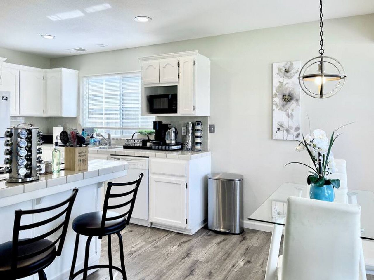A modern kitchen with white cabinetry, a central island with seating, and a dining area with a table and chairs.