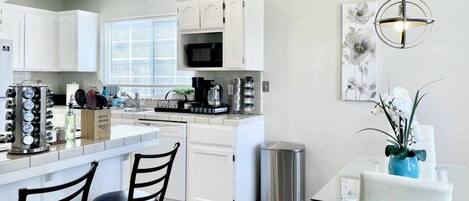 A modern kitchen with white cabinetry, a central island with seating, and a dining area with a table and chairs.