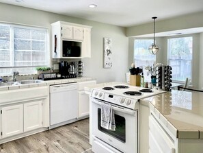 A modern kitchen with white cabinetry, a stove, and a sink. - Luxury 4BR Family Home w/ King Suite + Game Room (Chico)