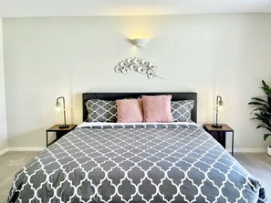 A bedroom with a bed, two bedside tables, a wall-mounted light fixture, and a potted plant.