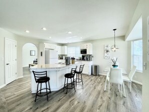 A modern kitchen with a central island, bar stools, and a dining area with a white table and chairs.