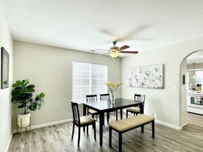 Un espace repas comprenant une table, des chaises, un ventilateur de plafond, une fenêtre et une plante.