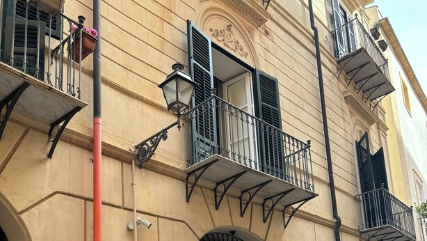 A vintage white Vespa scooter parked on a cobblestone street, a yellow building with ornate balconies and a black door, and a small outdoor seating area with tables and chairs. - Delightful and elegant apartment in the heart of Palermo. (Palermo)