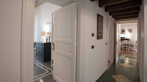 A hallway with a white door, a black dresser, and a lamp. There is a dining area with a table and chairs in the background. - Delightful and elegant apartment in the heart of Palermo. (Palermo)