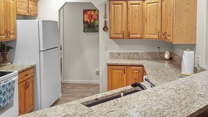 Eine Küche mit Holzausstattung, einer Granitarbeitsplatte, einem Kühlschrank und einem Spülbecken.