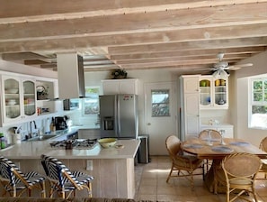A compact kitchen with white cabinets, a central island, and a dining area with wicker chairs. - Surf, Stay & Play DelMar 200 ft from Beach (Del Mar)