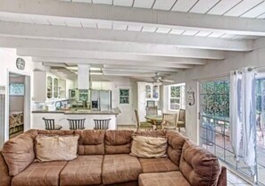 Relax in this spacious living area with a large sofa, high ceiling, and kitchen area.