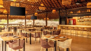 Een restaurant met rieten dak, rieten meubels en hangende rieten lampen.