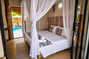 Ein Schlafzimmer mit Baldachinbett, Blick auf einen Pool und einem tropisch gestalteten Kissen.