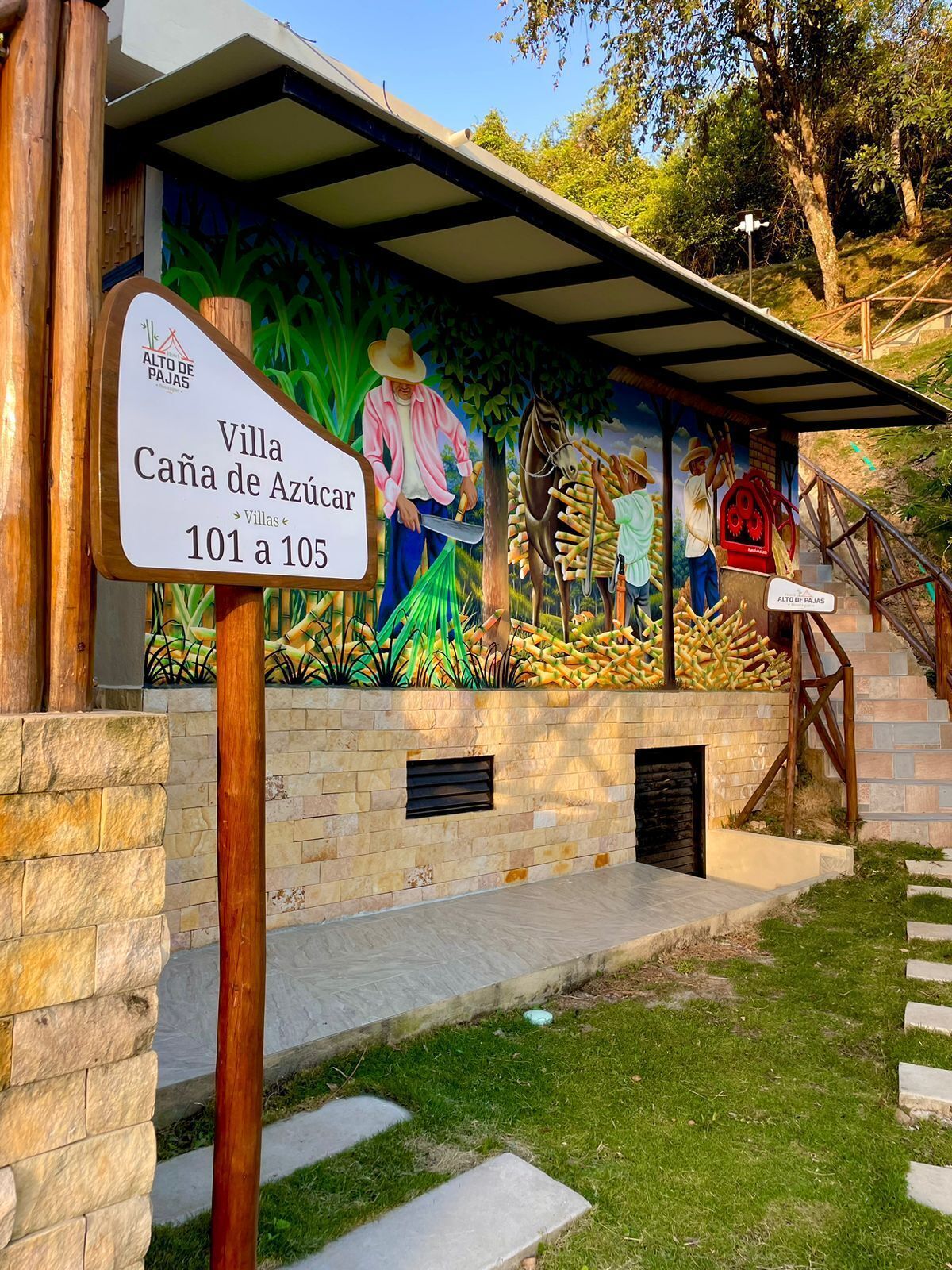 En villa kaldet 'Villa Caña de Azúcar' med et mural der viser landbrugsmotiver, stenvægge og en trappe til indgangen.
