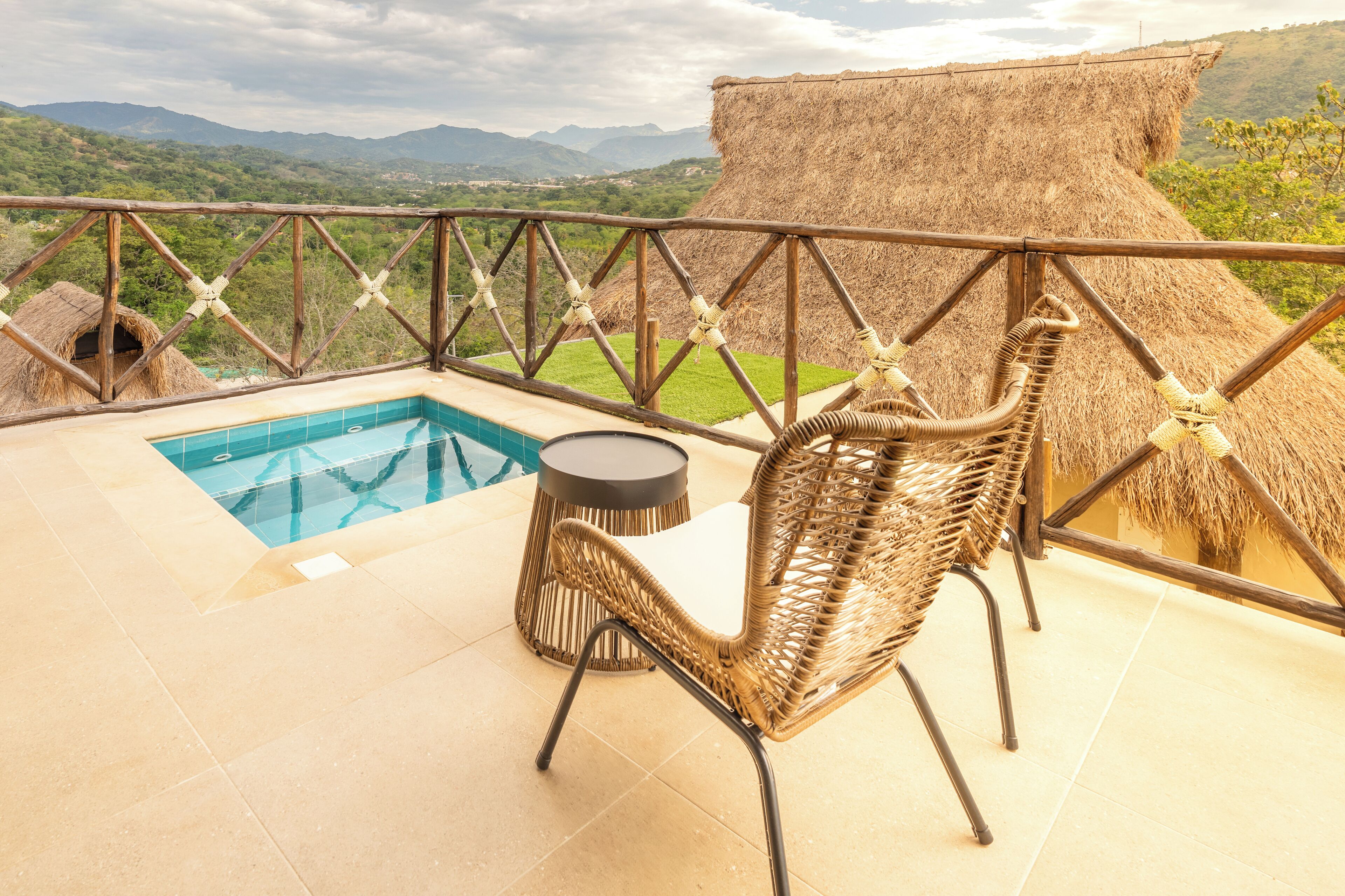 Zona de piscina con una silla de mimbre y una mesa redonda, con vistas a un paisaje montañoso.