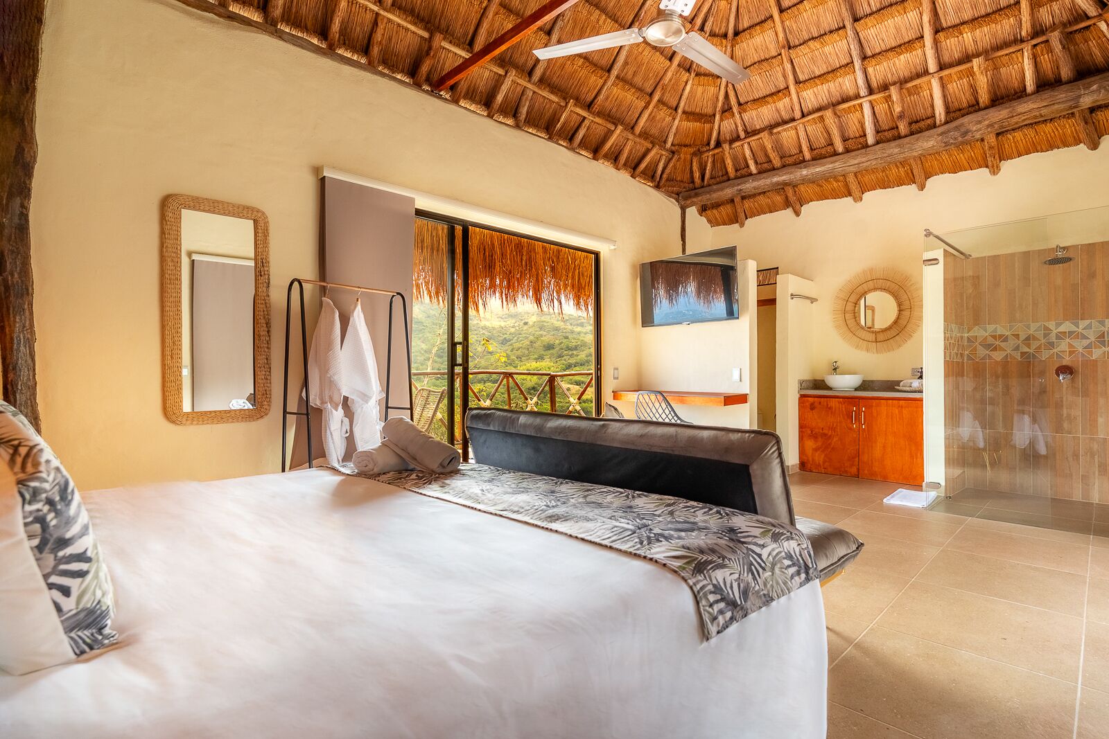 Un dormitorio con cama, televisión, baño con ducha y balcón con vistas.
