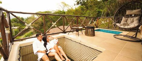 Una pareja descansando en una hamaca junto a una piscina, rodeada de mobiliario de mimbre y una terraza de madera.
