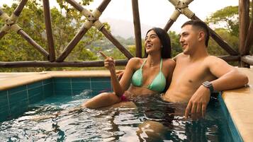 Una pareja en un jacuzzi con vistas a árboles y montañas.