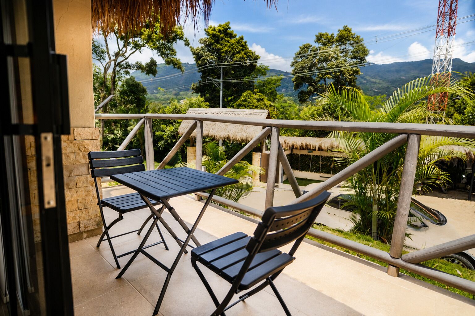 A balcony with a table and chairs, overlooking a lush landscape with trees and mountains.