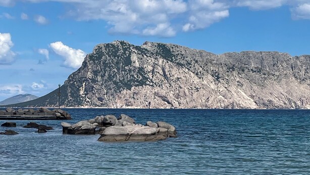 Un paisaje costero con aguas azules cristalinas, formaciones rocosas y una montaña distante.