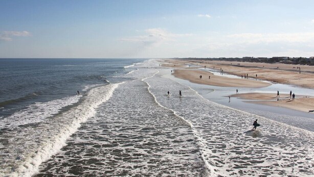 Uma praia com ondas, pessoas e céu claro.