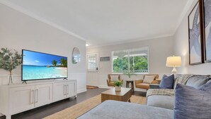 Uma sala de estar moderna com televisão de tela plana, sofá, mesa de centro e uma grande janela com vista para o verde.
