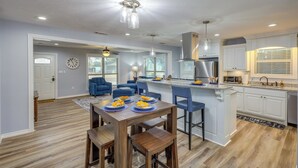 A modern kitchen with white cabinets, a stainless steel refrigerator, and a built-in microwave. There is a dining area with a wooden table and blue chairs.