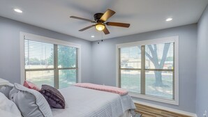 A bedroom with a bed, two windows, a ceiling fan, and a wooden floor.
