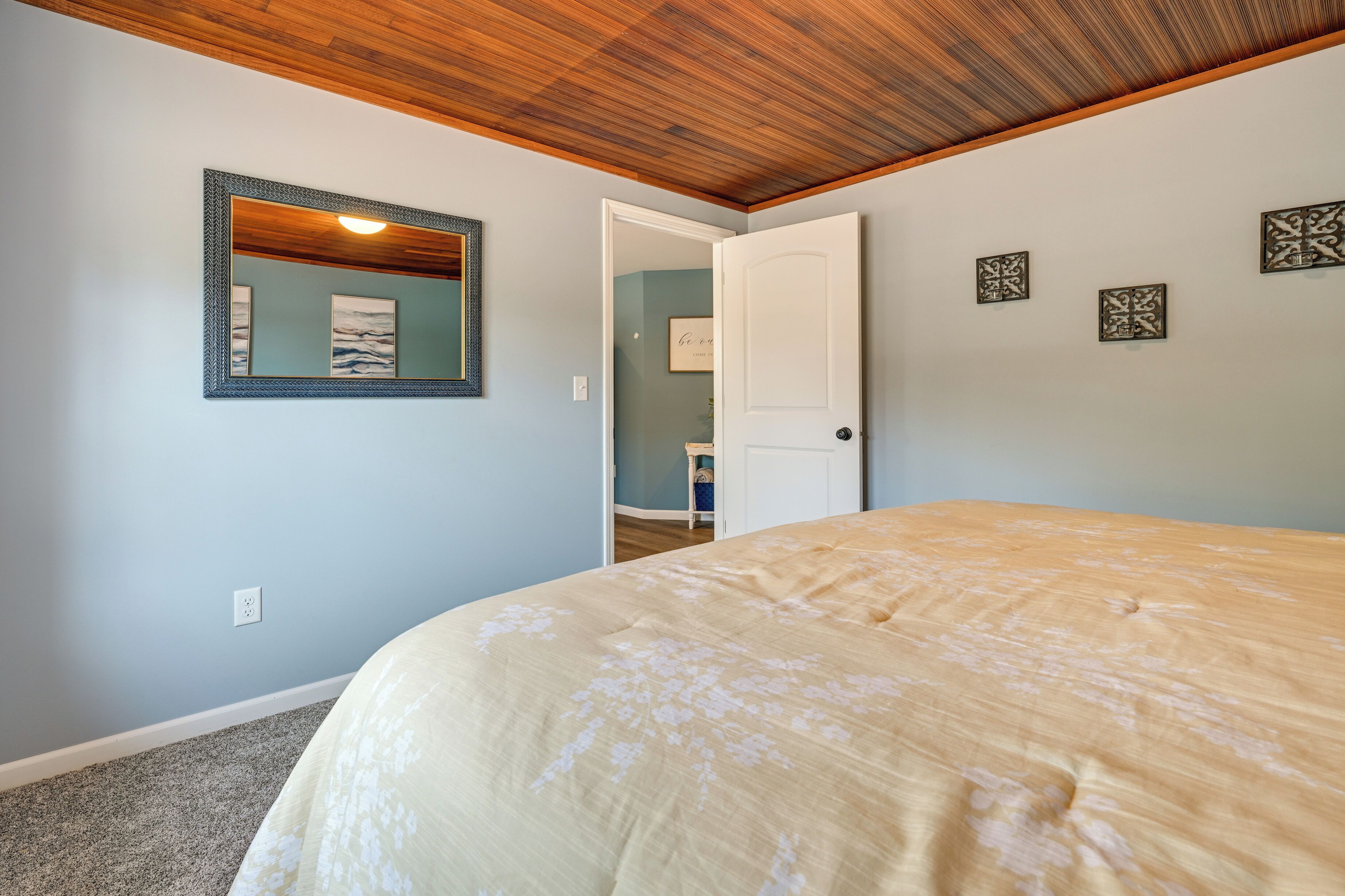 Ein Schlafzimmer mit einem Bett, einer Holzbalkendecke, einem Spiegel und einer Tür zu einem anderen Raum.