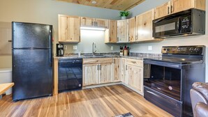 A kitchen with wooden cabinets, a black refrigerator, a microwave, and a stove. - Cozy Lake Wissota Escape w/ Community Dock! (Chippewa Falls)