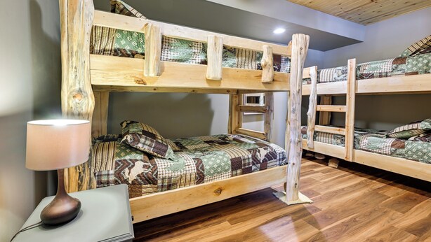 Habitación con literas de madera, una mesita de noche con lámpara y una colcha estampada.