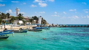 Escena costera con barcos amarrados cerca de un faro y un muelle que se adentra en el agua.