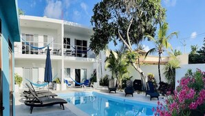 Un área de piscina con sillas de descanso, una hamaca y un edificio con balcones.