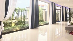A spacious hotel room with large windows, a modern chandelier, and a clean, reflective floor. - Oscar Villa (Da Nang)