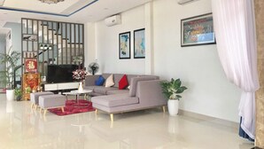 A modern living room with a sectional sofa, a TV, decorative plants, and artwork on the walls. - Oscar Villa (Da Nang)