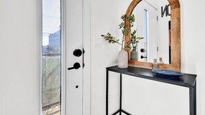 Een witte deur met een zwarte handgreep, een spiegel met houten lijst boven een zwart console tafeltje, en een uitzicht op een gebouw.