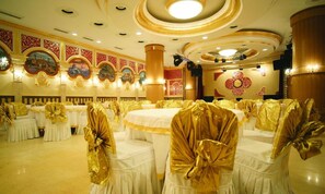 A banquet hall with round tables, white tablecloths, and chairs with golden sashes.