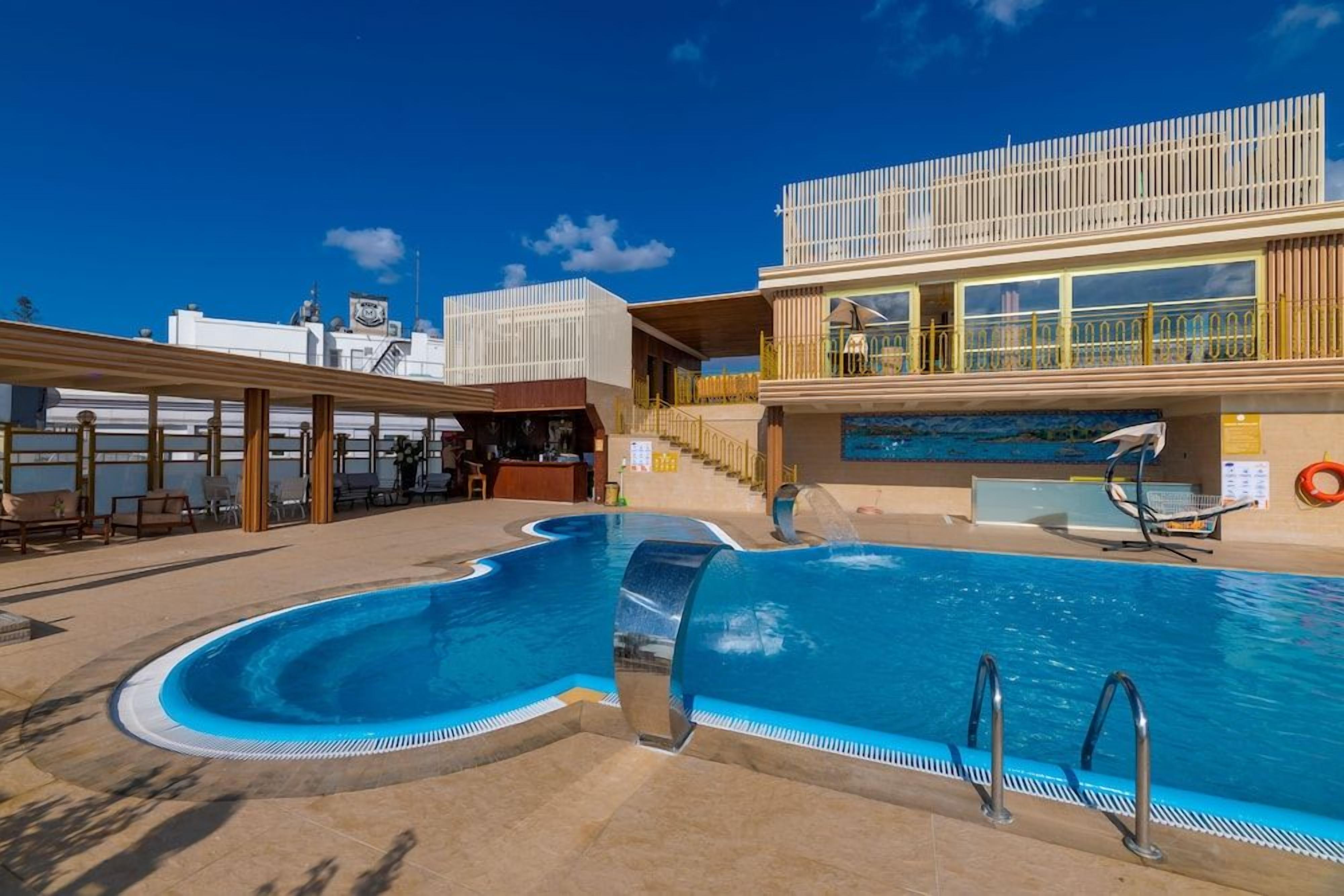 A swimming pool with a unique shape, a bar area, and a covered seating area.
