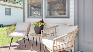 A porch with wicker chairs and a table, a potted plant, and a window with a view of a neighboring house. - Welcome to Casa de Campo! Your Home Away From Home (Saint Joseph)