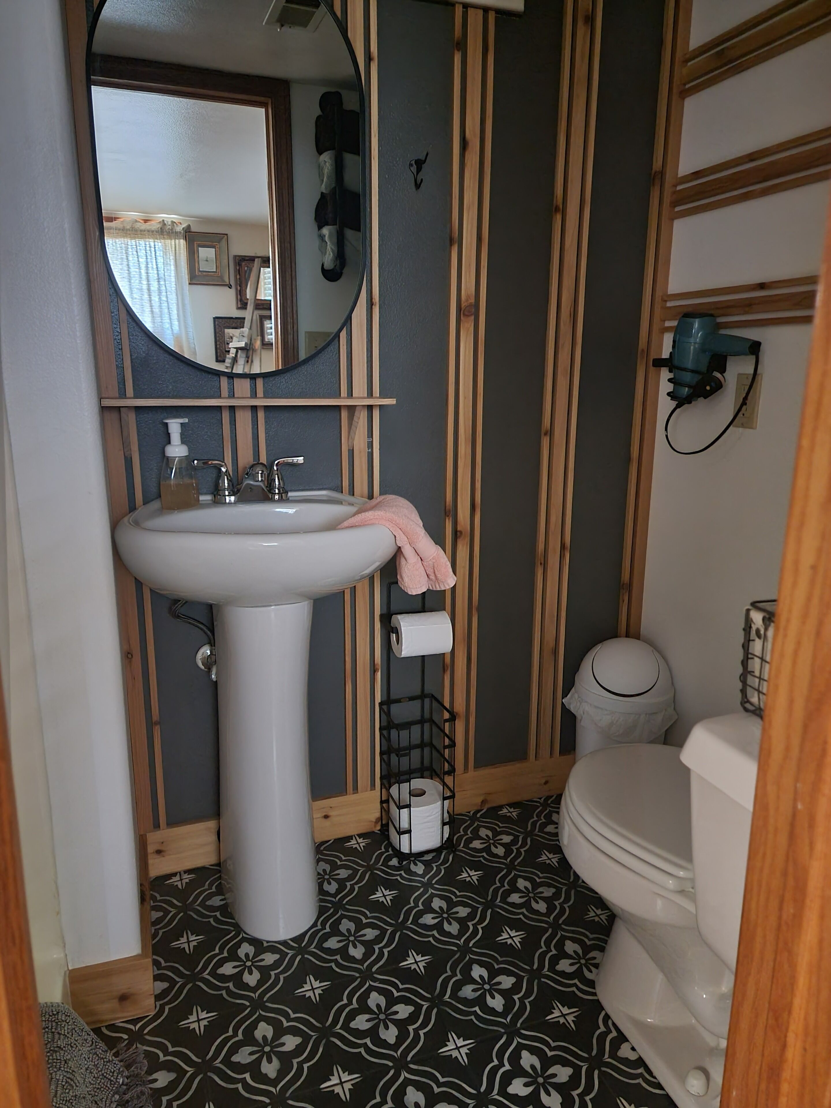 A bathroom with a white sink, a mirror, a toilet, and a patterned floor.