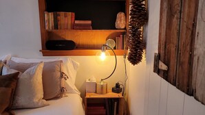 Une chambre confortable avec un lit, une table de chevet avec une lampe, une étagère avec des livres et une horloge, et un panneau mural rustique.
