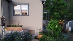 Une maison avec une fenêtre, un jardinier en bois rempli de fleurs et un jardin avec différentes plantes.