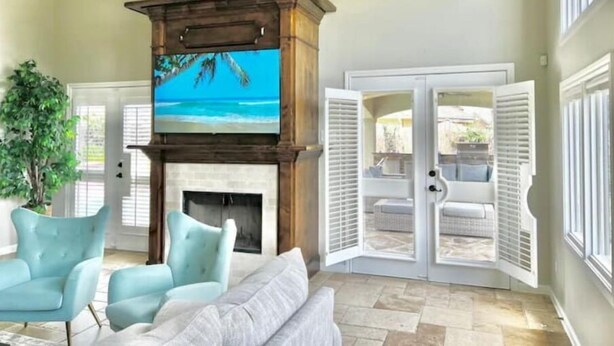 A living room with a fireplace, a television, and a view of the outdoors through a sliding door. - Premium Heated Pool House with Game Room (Houston)