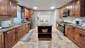 A kitchen with wooden cabinets, granite countertops, a central island, and a refrigerator. - Premium Heated Pool House with Game Room (Houston)