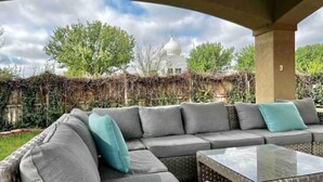 An outdoor seating area with a sofa and a table, a covered structure, and a view of a building with a dome. - Premium Heated Pool House with Game Room (Houston)