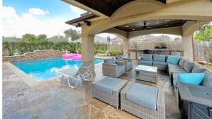 An outdoor patio with a pool, lounge chairs, and a built-in barbecue area. - Premium Heated Pool House with Game Room (Houston)