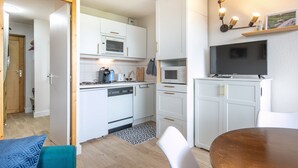 Een kleine keuken met witte kastjes, een magnetron, een broodrooster en een televisie op een standaard.