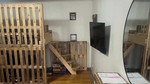 A room with a wooden floor, a TV mounted on the wall, a wooden bench, and a staircase. - Historic Mt. Iron Apartment (Mountain Iron)